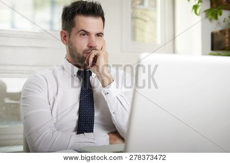 Businessman Looking Thoughfully While Sitting Behind His Laptop In The Office Care