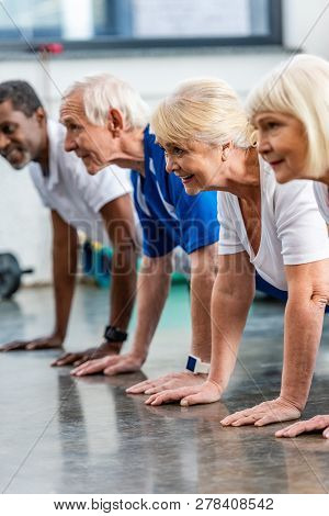 Smiling Mutiethnic Senior Athletes Doing Plank At Sports Hall