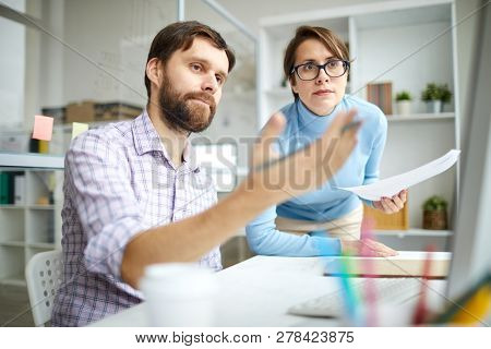 One of young economists or brokers pointing at computer screen while showing his colleague rate changes on website
