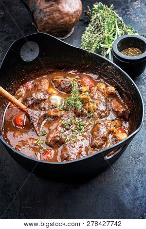 Traditional German braised pork cheeks in brown sauce with mushroom and carrots as closeup in a cast-iron pot