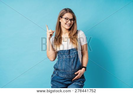 Pretty Young Pregnant Woman In Glasses And Denim Romper Pointing With The Index Finger Up A Great Id