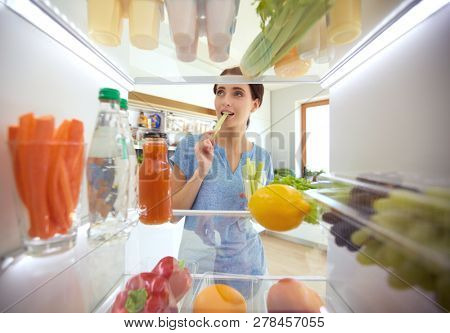 Portrait of female standing near open fridge full of healthy food, vegetables and fruits. Portrait of female
