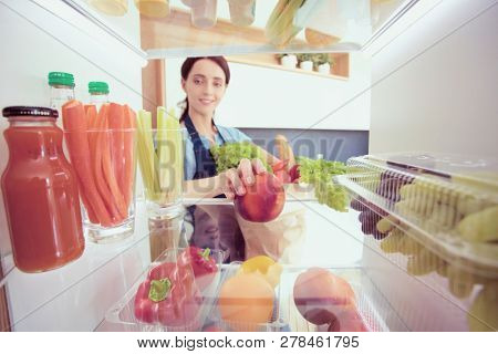 Portrait of female standing near open fridge full of healthy food, vegetables and fruits. Portrait of female