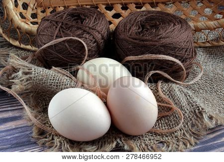View From Above Three Eggs Lie On A Beige Napkin On A Dark Background. Behind Yarn For Knitting And 