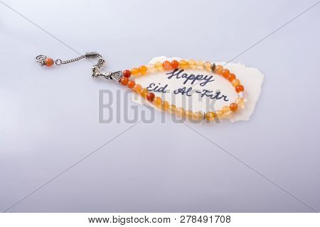 The Word Eid El Fitr  Written On Torn Paper Beside Prying Beads