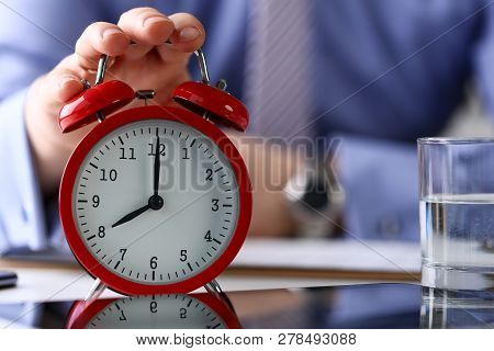 Male Arm In Suit And Tie Hold Up Red Alarm Clock In Office With Eight Oclock Early Morning Closeup. 