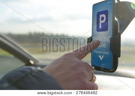 Driver using smartphone app to pay for parking in the paid parking zone in a city