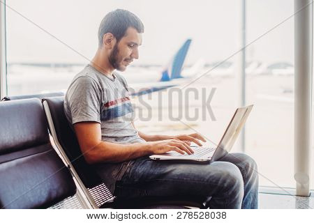 Young Man Using Laptop In Airport Terminal