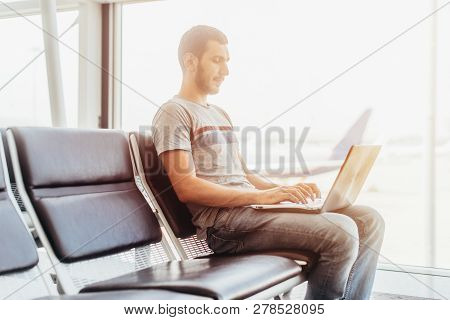 Young Man Using Laptop In Airport Terminal