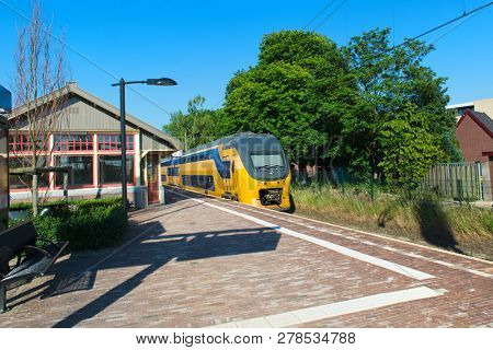 Dutch railway station with yellow train in little village Den Dolder