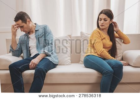 Young Wife Feeling Disillusioned Sitting Near Lying Husband