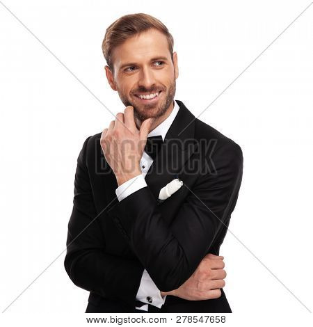 portrait of curious businessman looking to side and thinking while standing on whtie abckground and holding chin