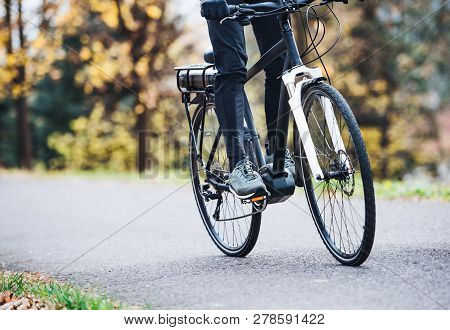 An Unrecognizable Man On Electrobike Cycling Outdoors On A Road In Park.