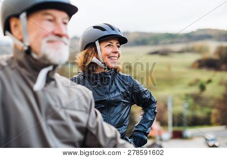 Active Senior Couple With Electrobikes Standing Outdoors On A Road In Nature.