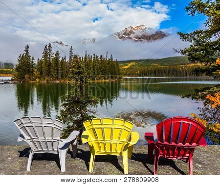 Three comfortable multi-colored deck chairs stand by the Piramid lake. Rocky Mountains of Canada. Concept of ecological, active and photo-tourism