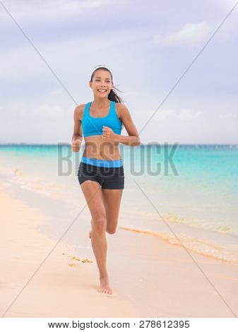 Active lifestyle young woman jogging on beach. Running barefoot on sand in Hawaii vacation travel Asian girl running on tropical holiday in blue activewear outfit.
