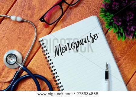 Top View Of Stethoscope,pink Eyeglasses,plant,pen And Notebook Written With Menopause On Wooden Back