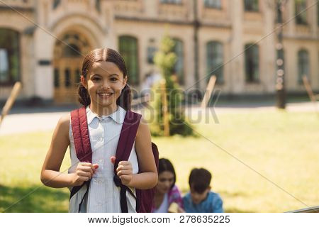 Beautiful Little Schoolgirl Standing With Rucksak In School Yard. Last School Dayd Before Summer Hol