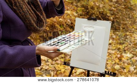 Close-up Of Young Girl Artist That Paints A Picture On The Easel In The Autumn Park