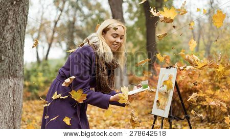 Blonde Girl Artist Draws Among Falling Leaves In The Autumn Park