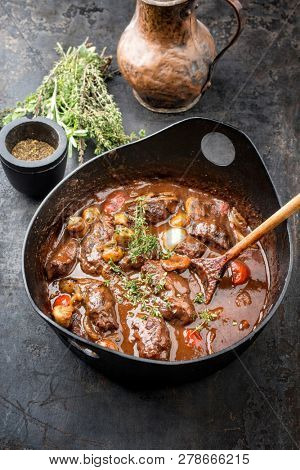 Traditional German braised pork cheeks in brown sauce with mushroom and carrots as closeup in a cast-iron pot 