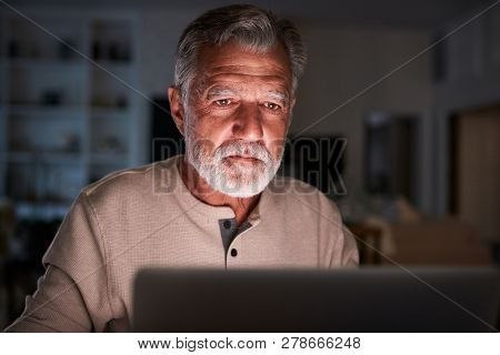 Senior Hispanic man checking his finances online at home using a laptop computer at night, close up