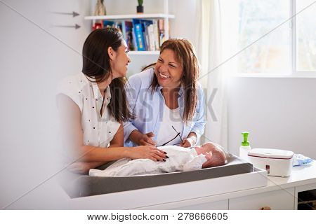 Millennial Hispanic mother and grandmother playing with baby son on changing table, selective focus