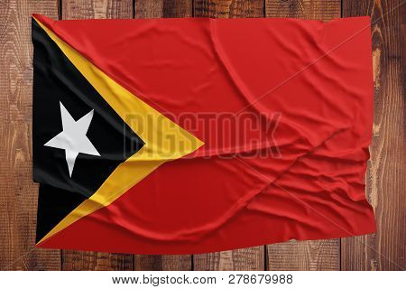 Flag Of East Timor On A Wooden Table Background. Wrinkled East Timorese Flag Top View.