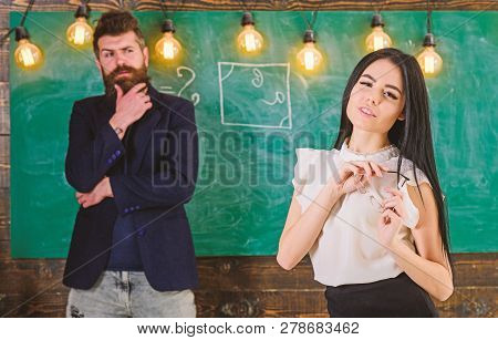 Man With Beard And Young Lady Teacher Stand In Classroom, Chalkboard On Background. Generation Conce