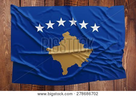 Flag Of Kosovo On A Wooden Table Background. Wrinkled Flag Top View.