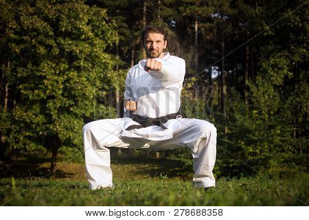 Karateist In White Kimono Is Practicing Martial Arts In Forest In Nature On Green Background.