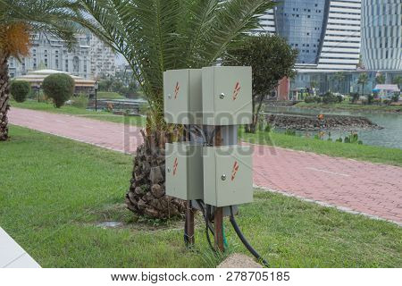 A Electric Box With Red-fed Power Cables Is Located In An Park Near The Footpath. An Electrical Safe
