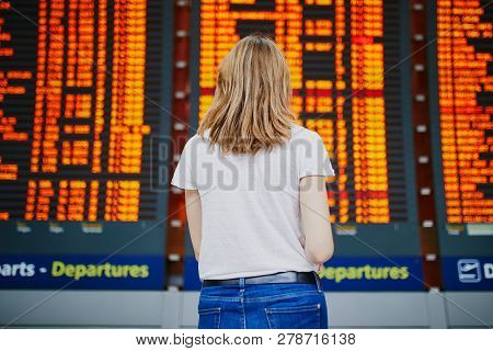 Young Woman In International Airport With Luggage Near Flight Information Display