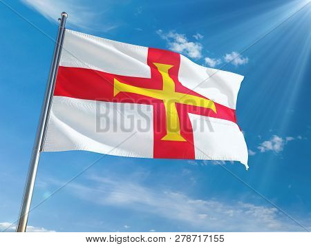 Guernsey National Flag Waving On Pole Against Sunny Blue Sky Background. High Definition