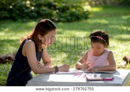 Mother Is Teaching Daughter Homework In Park,little Cute Girl Is Drawing With Color Pencil.