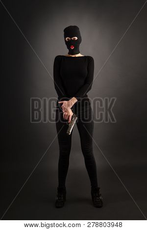Slim Sexy Girl In Dark Inconspicuous Clothes Hiding Her Face Under A Balaclava Hat With A Gun On A G