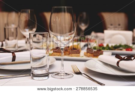 Festive Tableware With Glasses On A Table. Empty Glasses Stand Near Plates And Forks On Banquet Tabl