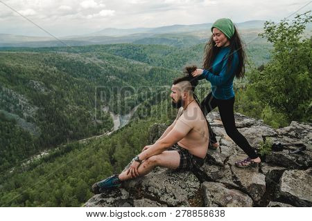 Asian Girl Doing Hair Style To Big Man On The Edge Of Rock In The Wild