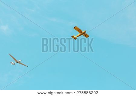 A Small Yellow Plane And Glider Flying Across The Blue Sky