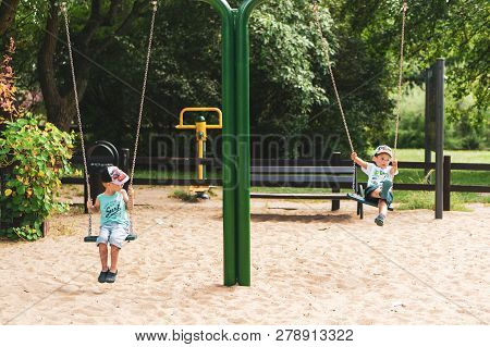 Poznan, Poland - July 29, 2018: Two Boy Sitting On A Swing At A Playground In The Cytadela Park. It 