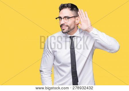 Young handsome business man wearing glasses over isolated background smiling with hand over ear listening an hearing to rumor or gossip. Deafness concept.