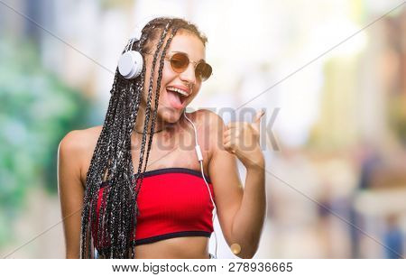 Young braided hair african american with birth mark wearing headphones over isolated background doing happy thumbs up gesture with hand. Approving expression looking at the camera