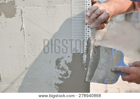 Hands Of An Old Manual Worker With Wall Plastering Tools Renovating House. Plasterer Renovating Outd