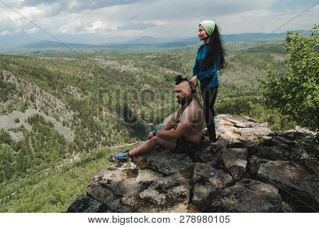 Asian Girl Doing Hair Style To Big Man On The Edge Of Rock In The Wild