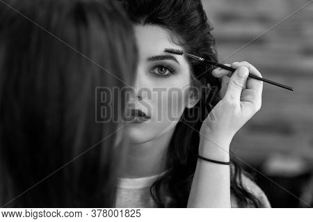 Black And White Portrait Of A Young Girl With Dark Long Hair, Whom The Stylist Does Makeup, Combing 