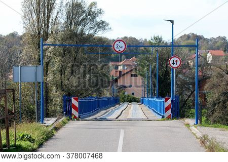 Entrance To Partially Renovated Wavey Old Wooden Bridge With New Blue Metal Frame On Each Side And S