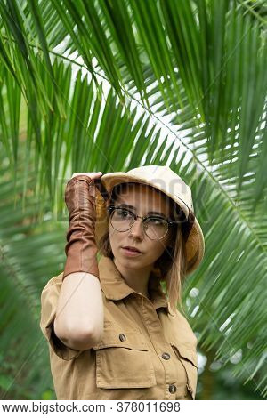 Woman Botanist Dressed In Safari Style In Greenhouse. Naturalist In Khaki Clothes, Leaver Gloves In 
