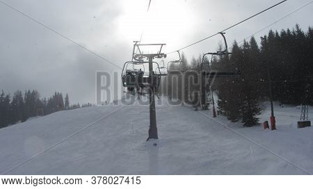 Shadow Of A Chairlift In Alpine Ski Area, Cloudy Gray Sky, Snow Falling Mountain Slope Covered In Sn