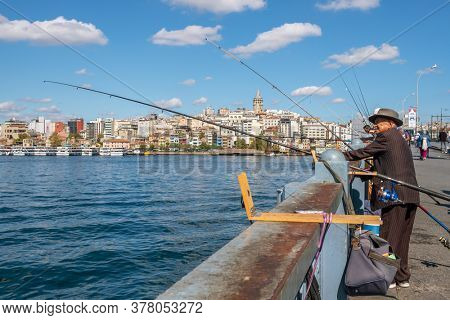Istanbul, Turkey - October 9, 2019: Unidentified turkish fisherman on Galata bridge with Galata tower at background in Istanbul
