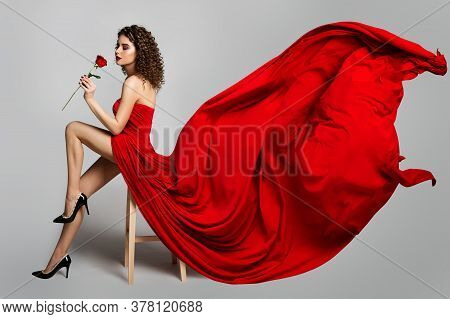 Beautiful Woman In Red Dress Smelling Roses Flowers, Fashion Model Studio Portrait On White, Flying 
